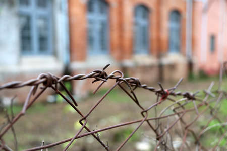 Rusty barbed wire of fence and out focus window of brick house.の写真素材