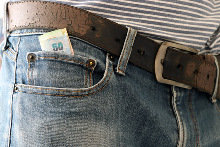 fifty baht banknote of Thailand in the mini pocket of blue jeans with belt.