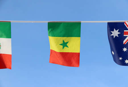 Mini fabric rail flag of Senegal, It is a tricolor consisting of three vertical green, yellow and red bands with a green star at the centre. It hanging on the rope cloth between the flag of other countries, on blue sky background.の写真素材