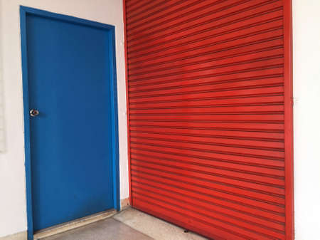 Two doors next to each other, Small blue wooden door for people to use,  big red metal door for Moving large stuff.の写真素材