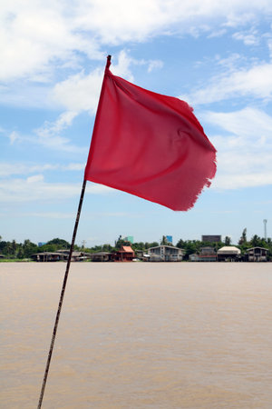 Red flag with blowing wind beside Chaophraya River, to signal let the boat to see that this is the shore.の写真素材