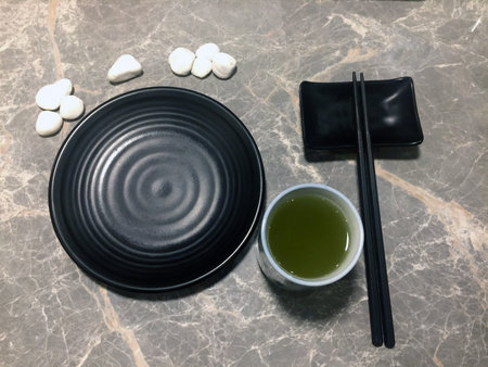 Green tea in a cup of tea and the set of black dish with black chopsticks, decorate with white small...