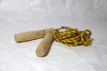 Rope for rope jump, yellow color with strips pattern in green - red and Wooden handle on white paper...