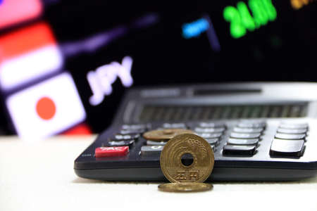 Japanese five Yen coins (JPY) on white floor with black calculator and digital board of currency exchange money background, the concept of finance.の写真素材