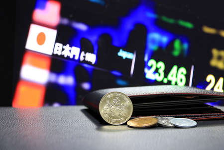 Japanese five hundred Yen coins on obverse (JPY) and pile of other Japanese coins on black floor with black wallet and digital board of currency exchange money background, the concept of finance.の写真素材
