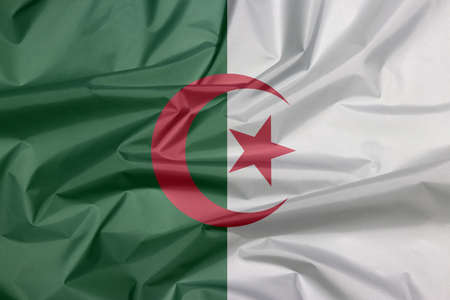 Fabric flag of Algeria. Crease of Algerian flag background, it is of two equal vertical bars, green and white, charged in the center with a red star and crescent.の写真素材