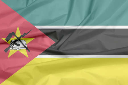Fabric flag of Mozambique. Crease of Mozambican flag background, horizontal green black yellow and small white with red triangle bearing the yellow star an AK-47 assault rifle and the bayonet on book.の写真素材