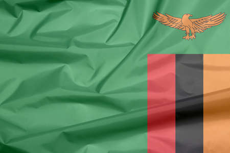 Fabric flag of Zambia. Crease of Zambian flag background, A green field with an orange colored eagle in flight over a rectangular block of red black and orange.の写真素材