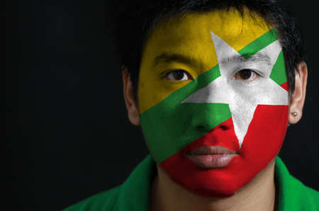 Portrait of a man with the flag of the Myanmar painted on his face on black background. red green and yellow color and white star.の写真素材