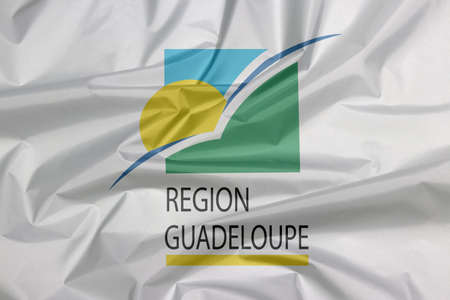 Fabric flag of Guadeloupe Region. Crease of Guadeloupe Region flag background. sun and bird on a green and blue square with the subscript REGION GUADELOUPE underlined in yellow.の写真素材