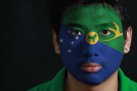 Portrait of a man with the flag of the Christmas Island painted on his face on black background, Blue and green diagonal color with white star, bird in gold and shape of the island.の写真素材