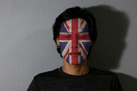 Portrait of a man with Union jack flag painted on his face and close eyes with black shadow on grey background. The concept of sport or nationalism.の写真素材