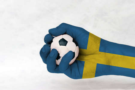 Mini ball of football in Sweden flag painted hand on white background. consists of a yellow or gold Nordic Cross on blue. Concept of sport or the game in handle or minor matter.の写真素材