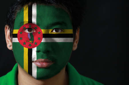 Portrait of a man with the flag of the Dominica painted on his face on black background, green field with cross of yellow, black and white, Sisserou Parrot on red disk and star.の写真素材