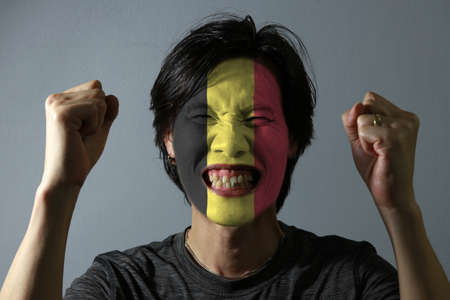 Cheerful portrait of a man with the flag of the Belgium painted on his face on grey background. The concept of sport or nationalism.の写真素材