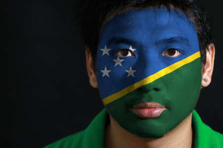 Portrait of a man with the flag of the Solomon Islands painted on his face on black background. The concept of sport or nationalism.の写真素材