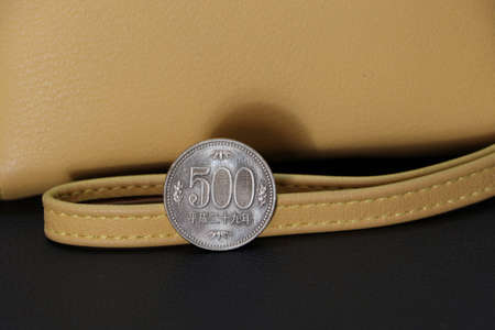 Japanese five hundred Yen coins on reverse (JPY) with sand color wallet on black floor, the concept of finance.の写真素材