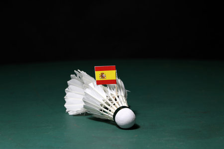 Mini Spain flag stick on used shuttlecocks on green floor of Badminton court with dark black...
