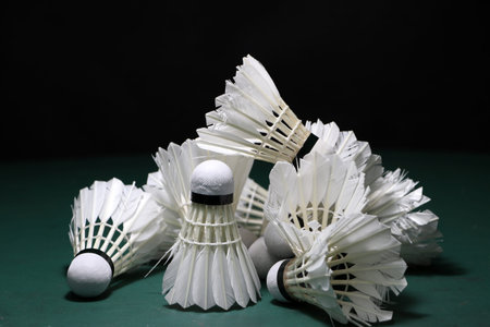 Heap of used shuttlecocks on green floor of Badminton court with dark black background.