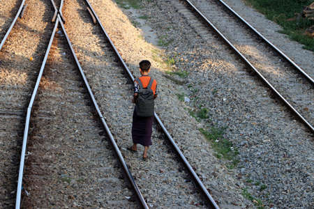 Yangon, Myanmar, Feb 20, 2019 : Back side of Myanmese man in short sleeve T shirt with backpack and Long Yi walking on the railroad tracks.のeditorial素材