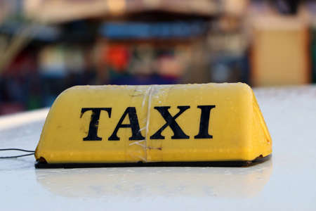Taxi light sign or cab sign in yellow color with black text and tied with transparent tape on the car roof at the street blurred background, Myanmar.の写真素材