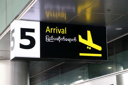 Arrival sign in english and Myanmar language with symbol of the plane landing in yellow on black color at the gate number 5, Installed from the ceiling.の写真素材