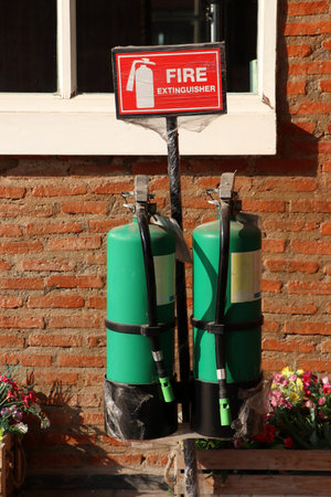 Two green fire extinguisher with the red sign and white text and symbolic icon on brick wall and window background.の写真素材