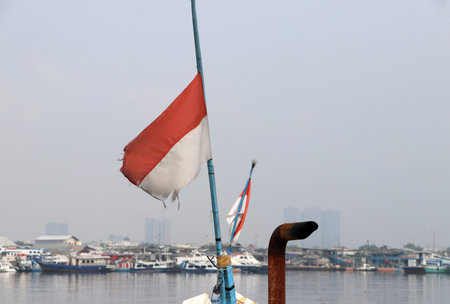 Indonesia old flag of fishing boat blow by the wind with background out focus sea harbor and boat.