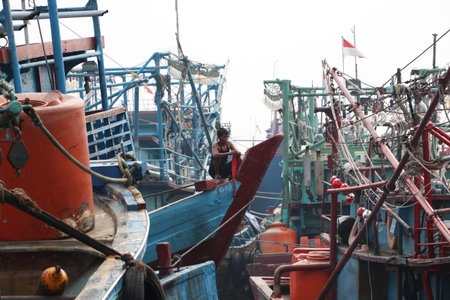 Jakarta, Indonesia May 6, 2019: Fisherman tying red cloth at prow of boat among many fishing boats moored in the port harbor.のeditorial素材