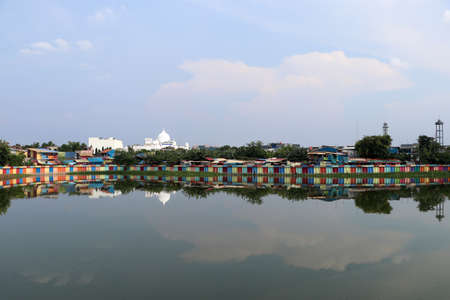 White muslim mosque in the rainbow village in Indonesia, colorful houses and colorful dam along the canal of slum, all that reflected in the water.のeditorial素材