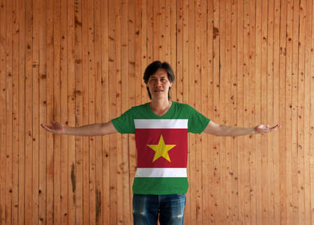 Man wearing Suriname flag color shirt and standing with arms wide open on the wooden wall background, green and red with large white border with the large yellow star.の写真素材