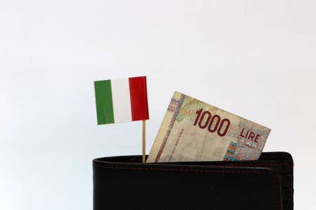 One thousand Lire of Italy banknote and mini Italia nation flag stick on the black wallet with white background. Concept of finance or currency.の写真素材