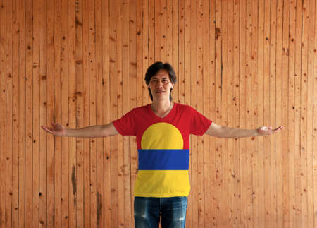 Man wearing United States Minor Outlying Islands flag color shirt and standing with arms wide open on the wooden wall background. red blue and yellow color.の写真素材