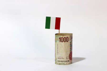 Rolled banknote money one thousand Lire Italy and stick with mini Italia nation flag on white background. Concept of financial business.の写真素材