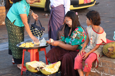 Yangon, Myanmar - Feb 25, 2019 : Myanmese female street vendor and daughter sitting and peeling...