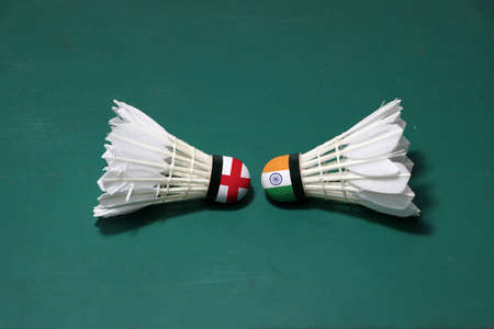 Two used shuttlecocks on green floor of Badminton court with both head each other. One head painted with England flag and one head painted with the India flag, concept of badminton competition.の写真素材