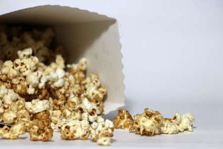 Heap of chocolate and caramel popcorn from paper box on the white floor. It is the corn of a variety with hard kernels that swell up and burst open with a pop when heated.の写真素材