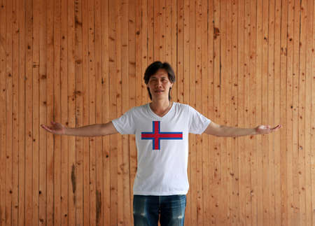 Man wearing Faroe Islands flag color shirt and standing with arms wide open on the wooden wall backgroundの写真素材