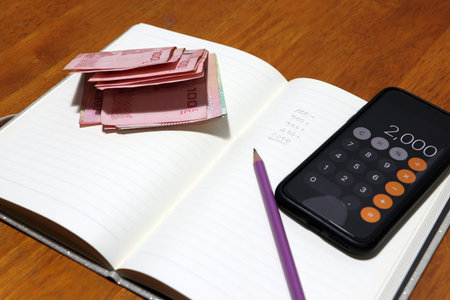 Writing the amount of money in the book by pencil with calculator and a certain amount of Thai baht....