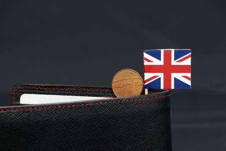 One Penny British decimal coin money and mini Union Jack flag stick on the black wallet with dark background. Concept of finance or currency.の写真素材