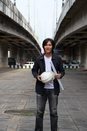 Civil engineer man standing with white helmet and project drafts while in hand on parallel expressway background.の写真素材