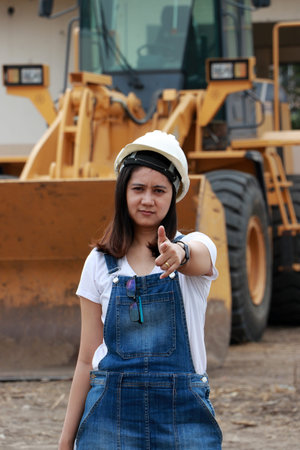 Female civil engineer or architect with white helmet and project drafts while in hand standing at the work area with out focus Alloy Bulldozer Truck with Front Loader Truck Engineering Construction Car Vehicle.の写真素材