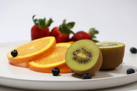 Cut in half of kiwi fruit put together without focus The thin round pieces of orange slices, strawberry and blueberry on the white round dish.の写真素材