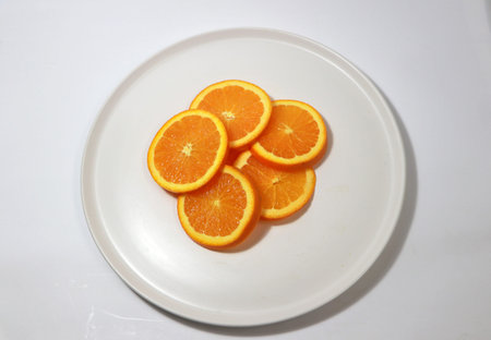 The thin round pieces of orange slices pile together on the white dish.