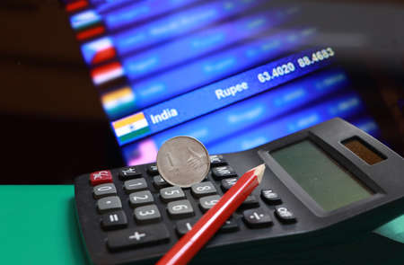 One Rupee coin of India and pencil on the calculator with digital board of currency exchange money background. Concept of finance or currency.の写真素材