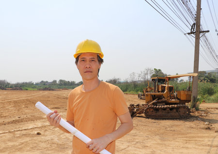 Male civil engineer or architect wear yellow helmet and project drafts while in hand standing on...