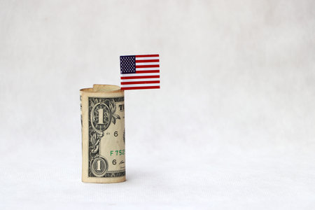 Rolled one US dollar banknote of America and mini USA flag on the white floor. Concept of saving money or finance.の写真素材
