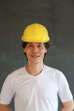 Male civil engineer or architect with yellow helmet and wear white T-shirt on dark grey background.