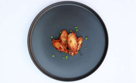 Grilled chicken wings in the black round plate on the white floor. Sprinkled with spring onions.の写真素材
