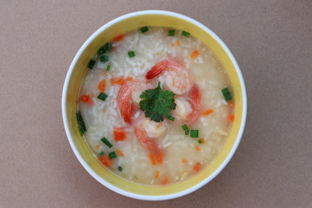 Rice congee mixed with shrimp in the round bowl on the brown floor. Sprinkled with spring onions and...